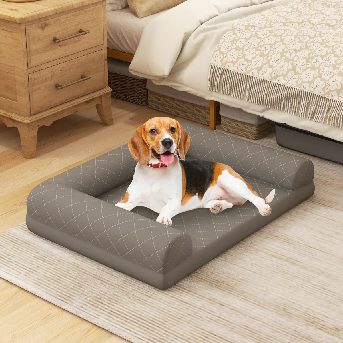 Grey quilted bolster dog bed on a rug beside a bed, with a beagle lying on it