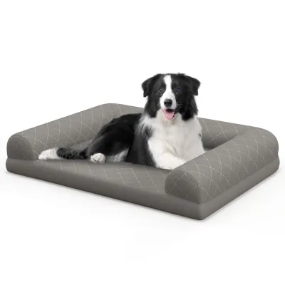 Grey quilted bolster dog bed on a white background with a border collie resting on it
